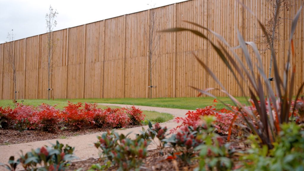 Landscaped footpath and planting in front of a completed timber noise barrier within a residential development.